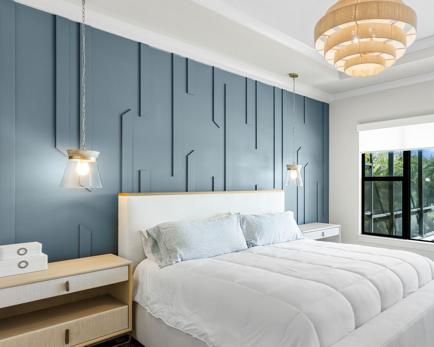 Bedroom with a navy geometric trim accent wall behind an upholstered bed, hanging pendant lights and a tiered chandelier